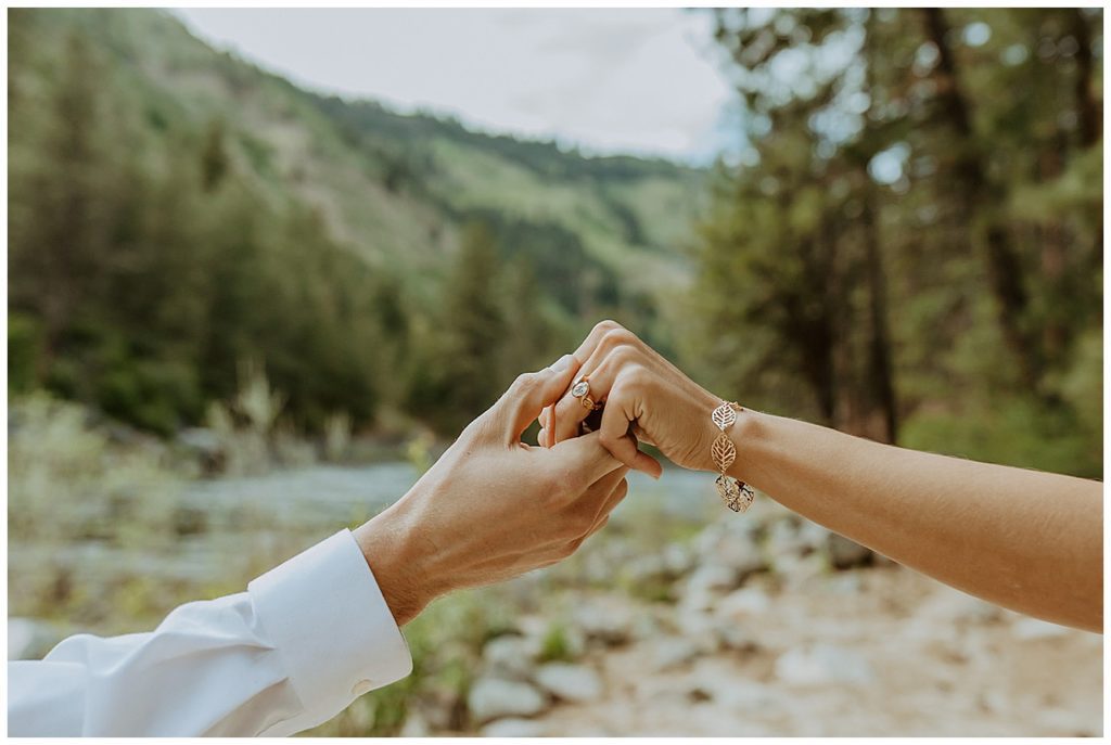 a close up of two people showing their engagement ring with idaho mountains in the background